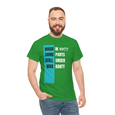 Humorous aging t-shirt with "Made In Some Parts Still Under Warranty" slogan, vintage style, green color.