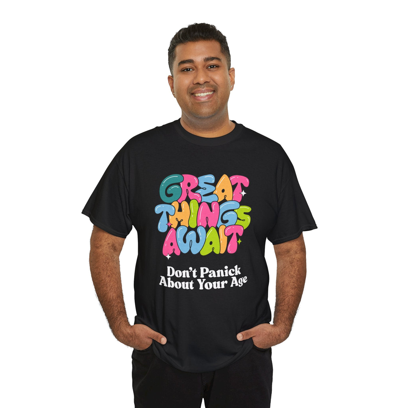 Colorful "Great Things Await" t-shirt with positive message, cheerful font, and multi-colored letters, worn by a smiling person.
